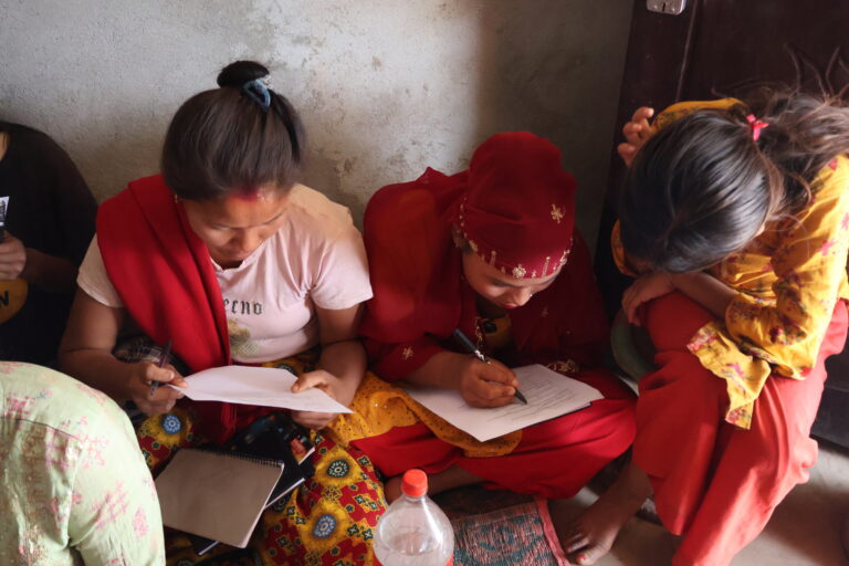 Four ladies wearing bright clothes sat down on a floor being taught by the three sisters - GESI (Gender Equality & Social Inclusion) Workshop for 25 Chepang women.