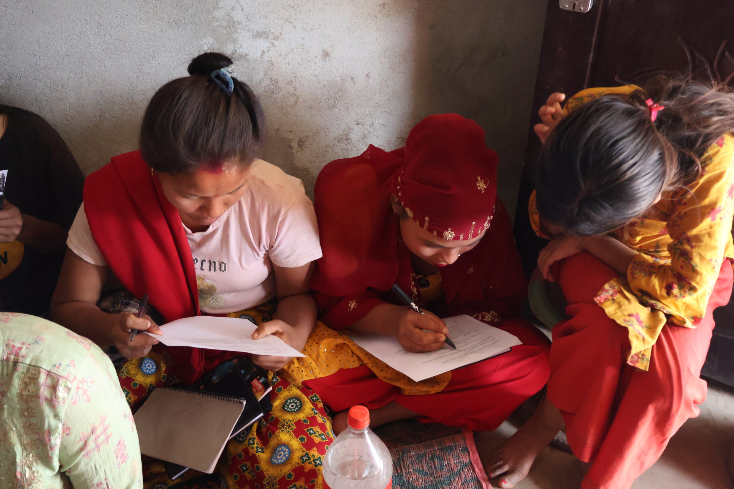 Four ladies wearing bright clothes sat down on a floor being taught by the three sisters - GESI (Gender Equality & Social Inclusion) Workshop for 25 Chepang women.