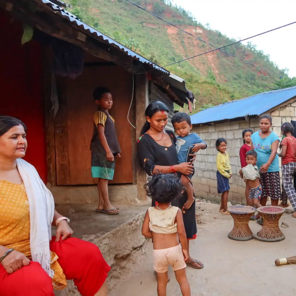 Families and children gathered outside hillside homes in Dhading, Nepal.