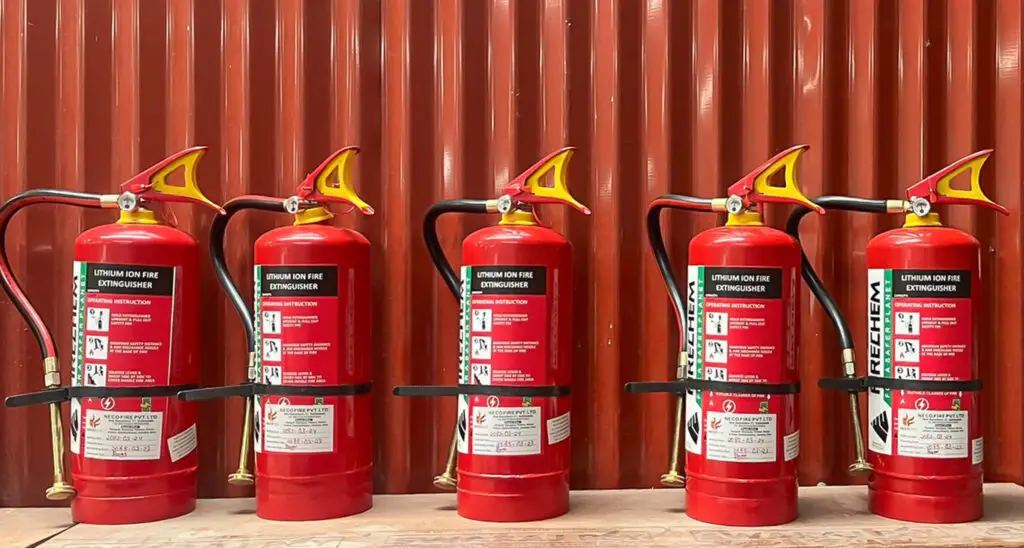 Five red fire extinguishers sitting on a table with a red corregated background wall for the NEVI Factory