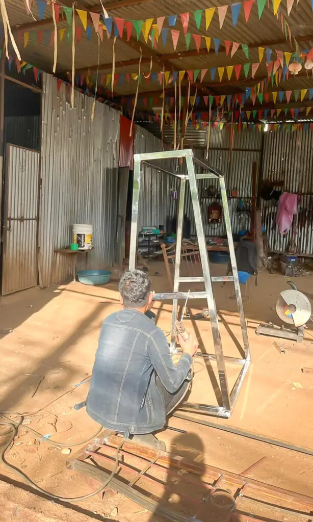 Man sitting on the floor holding a screwdriver whilst making a prototype crade holder for the batteries in the NEVI Factory.