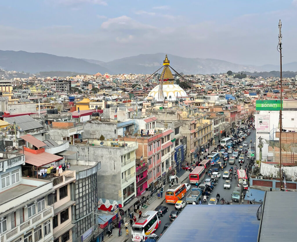 View over Kathmandu city with the Boudhanath Stupa in the distance and busy traffic below.