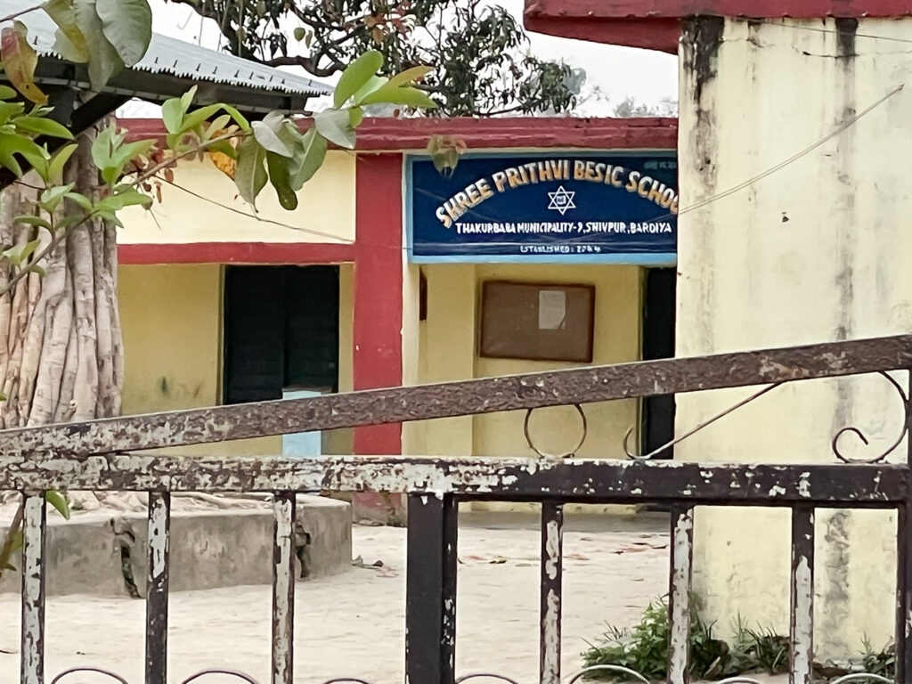 Entrance of Shree Prithvi Basic School in Bardiya, Nepal, with a blue sign above the doorway.