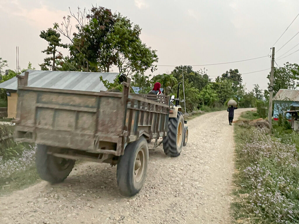 Tractor with trailer driving along an unpaved rural road in Bardiya, Nepal, with a person walking ahead.