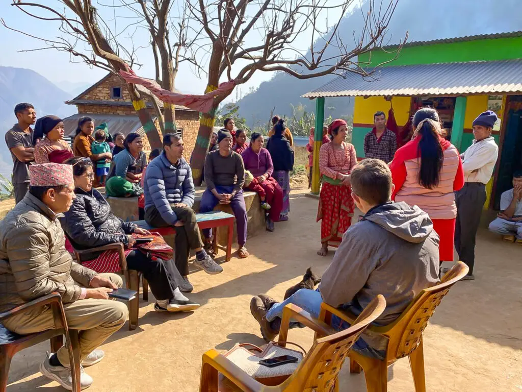 Community meeting in Dhading, Nepal, with local residents and project team members gathered outdoors to discuss needs and priorities.