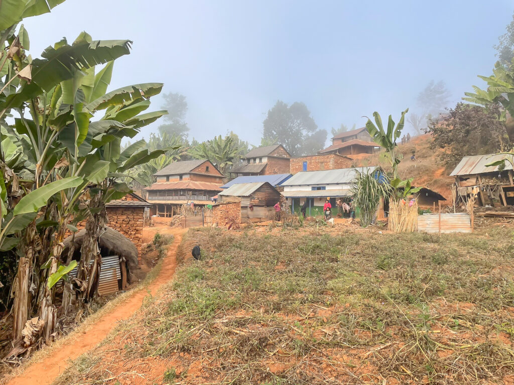 View of traditional hillside village homes surrounded by farmland and banana trees at the Dhading pilot site in Nepal.