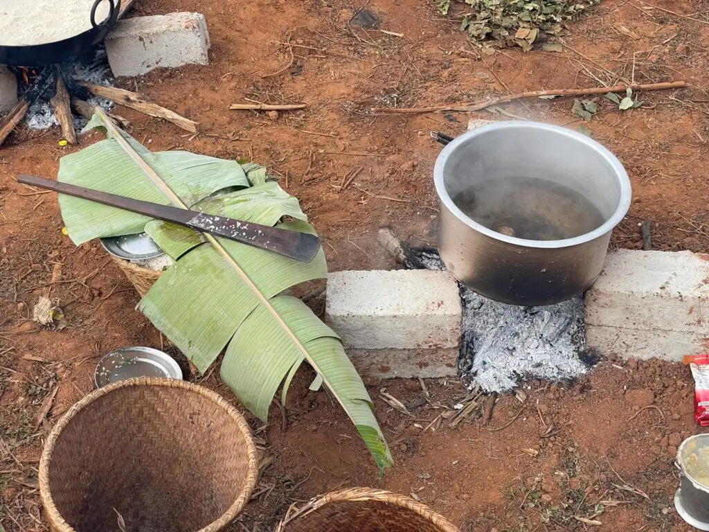 Outdoor cooking setup in Nepal with a metal pot on an open fire and banana leaves used for preparation.